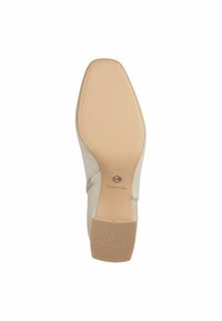 Zapato de ante beige con suela de goma, que presenta un diseño texturizado y un logo circular cerca del talón. Diseño plano apto para uso casual.