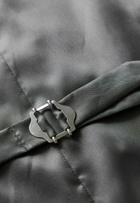 Material textil gri, cu o textură netedă, având un detaliu cu cataramă metalică, fixat de un design cu închidere argintie în centru.