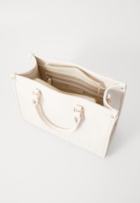 Väsk av vit pebblad läder med detaljer i guldton, dubbla handtag upptill, dragkedjefack och emblematisk logga på framsidan.