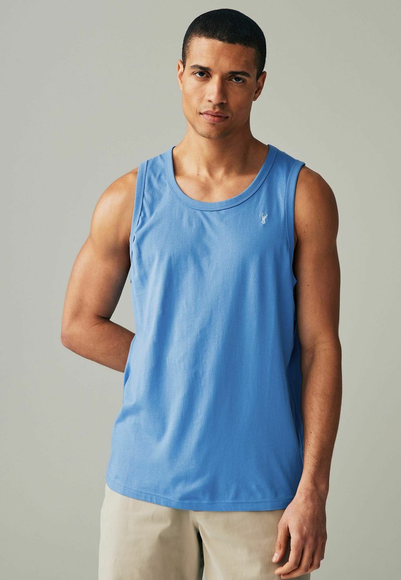 Blå tanktop lavet af blødt stof, med rund halsudskæring og et lille emblem på venstre bryst. Glat tekstur og klassisk pasform.