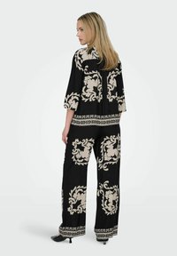 Ensemble noir en deux pièces comprenant un haut ample à manches trois-quarts et un pantalon à jambes larges, tous deux ornés de motifs floraux crème et d'accents.