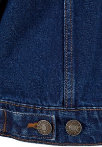 Dettaglio ravvicinato di un tessuto di denim blu scuro con cuciture arancioni e due bottoni metallici incisi con "Urban Classics."
