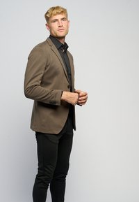 Brun figureret blazer med skræddersyet design, notch-lapper og enkelt knaplukning, parret med slim-fit sorte bukser. Glat stofstruktur.