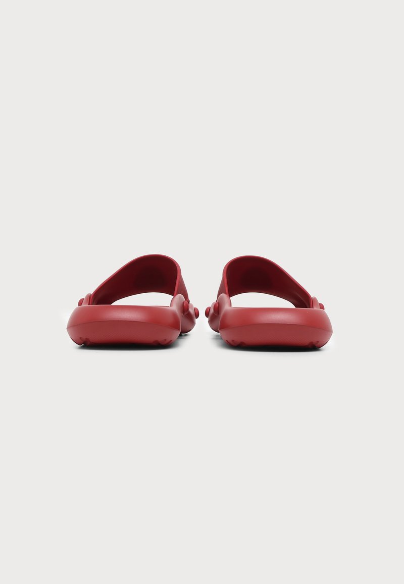 Paar rote Slides-Sandalen von hinten auf einem schlichten hellen Hintergrund gesehen.