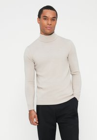 Beżowy sweter z golfem wykonany z miękkiego, dzianinowego materiału, z długimi rękawami i dopasowanym krojem. Subtelne logo na klatce piersiowej.