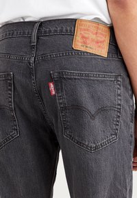 Jeans de mezclilla gris oscuro con un parche de cuero en la cinturilla, etiqueta roja de Levi's en el bolsillo trasero y un clásico diseño de cinco bolsillos.