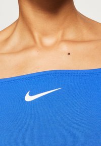 Blå ribbad linne med vid halsringning, med en vit Nike-logga på bröstet, slät textur och inga synliga detaljer eller accenter.