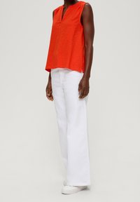 Červený bezrukávový top s výstřihem do V a jemnou texturou, zkombinovaný s bílými širokými džíny a bílými teniskami.