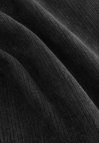 Černá texturovaná tkanina s diagonálním žebrovaným vzorem, ukazující zavěšené záhyby, které odhalují měkkost a hloubku barvy.