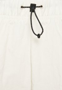 White elastic waist shorts made of lightweight fabric, featuring a black adjustable drawstring and metal grommets for securing.