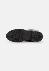 Suela de bota de goma negra con un patrón de talla profundo, que incluye surcos horizontales y diagonales para la tracción. Construcción duradera y superficie texturizada.