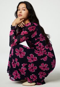 Florale midi-jurk met een marineblauwe basis en grote roze bloemen, lange mouwen en een vloeiende silhouet. Gladde, lichte stof met een zachte textuur.