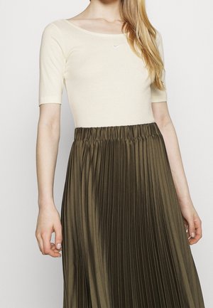 Cremefarvet top med korte ærmer og rund halsudskæring, kombineret med et højtaljet, plisseret nederdel i olivengrøn. Enkelt Nike-logo på toppen.