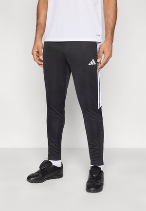 Pantalon de sport noir à coupe slim avec des bandes blanches latérales, doté d'une ceinture élastique et d'une texture de tissu douce et lisse.