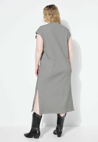 Schwarz-weiß gestreiftes, knielanges Kleid mit kurzen Ärmeln und seitlichen Schlitzen, kombiniert mit schwarzen, gepunkteten Cowboy-Stiefeln.