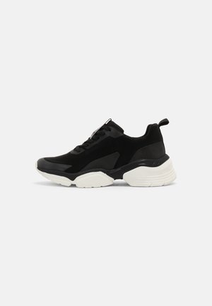Czarny, niski sneaker z grubą białą podeszwą, sznurowaniem z przodu i uchwytem na pięcie, pokazany z boku na jednolitym tle.