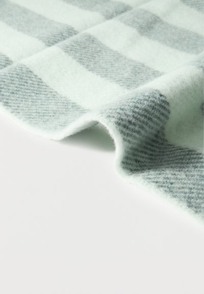 Μαλακό γκρι και λευκό καρό ύφασμα με αφράτη υφή, εμφανίζεται ελαφρώς διπλωμένο σε απλή λευκή επιφάνεια.