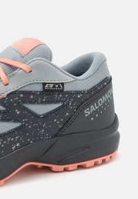 Los zapatos de exterior impermeables cuentan con una parte superior de malla gris con acentos en gris oscuro, cordones rosas y un detalle moteado en el costado.