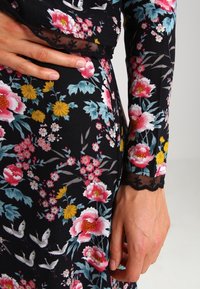 Abito floreale con tessuto nero decorato da fiori rosa, gialli e blu; raffinati dettagli in pizzo sulle maniche; vestibilità leggermente comoda; superficie testurizzata.