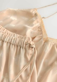 Ensemble de lingerie en satin beige doux avec motif floral, caraco bordé de dentelle et short à taille élastique avec cordon de serrage.