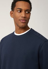 Marineblaues Sweatshirt mit Rundhalsausschnitt, strukturiertem Stoff und dezentem gesticktem Logo auf der Brust. Lässige Passform und Schulternahtdetails.