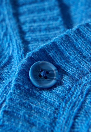 Blauer, gestrickter Pulloverstoff mit einem strukturierten Muster, versehen mit einem runden, blauen Knopf mit vier Löchern und einem marmorierten Design.