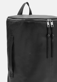 Sac à dos en cuir noir de forme arrondie, avec deux zips et une poignée supérieure. Il dispose d'une texture lisse et de détails de couture minimaux.