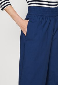 Marineblauwe broek met een elastische tailleband en zijzakken, gemaakt van lichtgewicht stof, met een soepele textuur en een eenvoudig ontwerp.