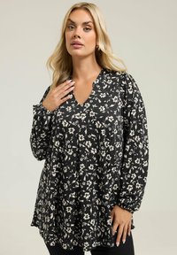 La blusa nera a fiori presenta un collo a V, maniche lunghe a palloncino con polsini elasticizzati e una vestibilità rilassata con motivi floreali beige in tutta la superficie.