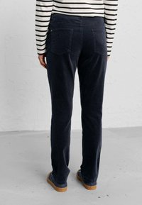 Marina kordflersbyxor med en figurnära passform, som har två bakfickor och en mjuk textur. Bärs tillsammans med en svart och vit randig långärmad skjorta.