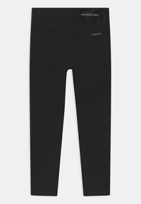 Jeans de mezclilla negra con un diseño ajustado, cinco bolsillos y una etiqueta con el logotipo de Calvin Klein Jeans en la cintura. Textura suave, piernas rectas.