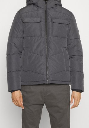 Ciemnoszara pikowana zimowa kurtka z frontowym zamkiem błyskawicznym, dwoma kieszeniami na klapie na piersiach, dwiema bocznymi kieszeniami oraz kapturem, noszona z dopasowanymi szarymi spodniami.