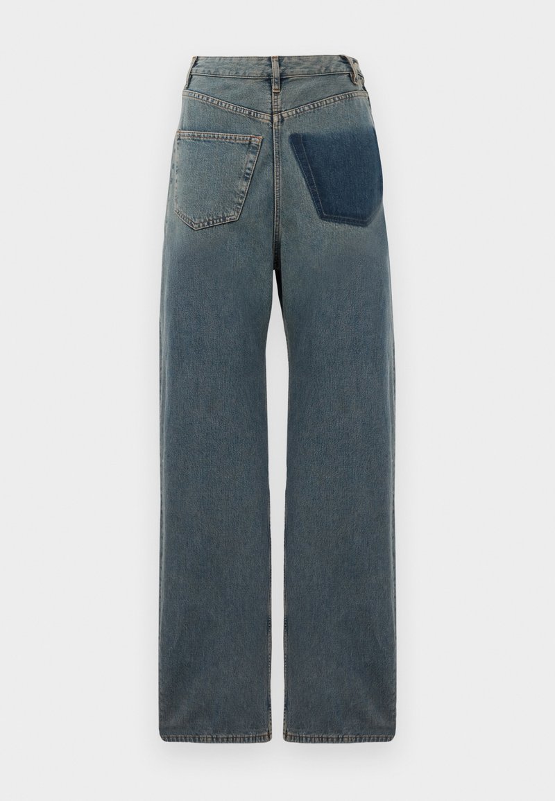 Jean large en denim, avec une teinte bleue claire, deux poches arrière et une poche plaquée d'une teinte bleue plus foncée sur le côté droit.