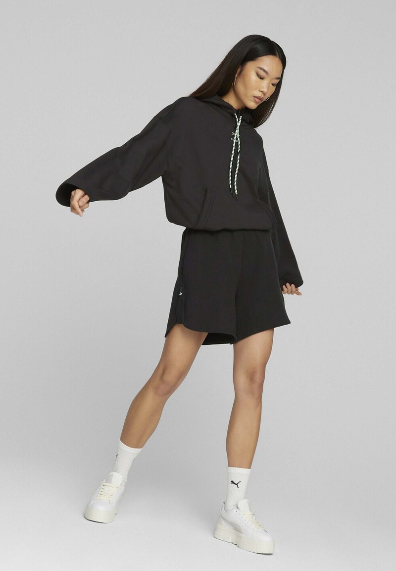 Svart hettegenser med lommer foran, kombinert med svarte shorts. Har snøring med et hvitt og grønt mønster. Hvite sneakers.