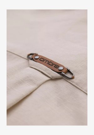 Beige fabric with a textured finish featuring a leather label with the word "ombre" in embossed lettering and silver metal accents.