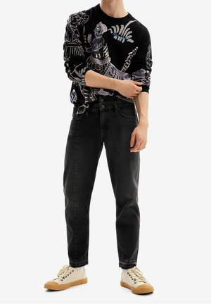 Maglione nero con stampa grafica, jeans neri a vita alta e sneakers beige. L'outfit presenta una vestibilità rilassata e design dettagliati.