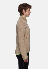 Veste en polaire beige avec un motif texturé. Elle présente des accents vert vif sur le col et les poignets, avec une poche zippée sur le côté.