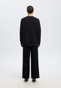 Cardigã preto e felpudo com bainha arredondada e mangas compridas. Combinado com calças largas pretas e sapatos de salto alto pontiagudos.