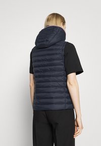 Granatowa pikowana kamizelka z kapturem, z pikowanymi panelami i gładkim wykończeniem. Noszona na czarnej koszulce z krótkim rękawem, zestawiona z luźnymi czarnymi spodniami.