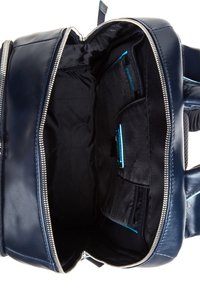 Interior de mochila de cuero marino con cierre de cremallera. Presenta forro de tela negra, múltiples compartimentos y acentos en turquesa contrastantes.