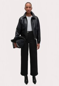 Czarna skórzana kurtka bomberka na szarej koszuli, zestawiona z czarnymi spodniami z wysokim stanem. Uzupełniona plecioną czarną torebką i szpiczastymi butami.