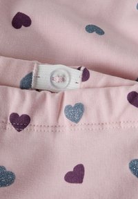 Różowy materiał z nadrukiem fioletowych i błyszczących niebieskich serc posiada biały elastyczny pas z regulatorem i przezroczystym guzikiem.