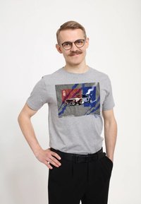 Šedé bavlněné tričko s grafikou auta na texturovaném pozadí s červenými a modrými akcenty. Krátké rukávy a kulatý výstřih.