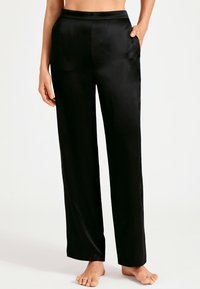 Pantalons en satin noir avec une coupe droite, présentant une texture lisse et des poches latérales. La ceinture est plate et ajustée. Sans motifs ni ornements.
