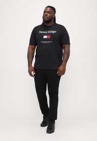 Must matte must shirt, mille "Tommy Hilfiger" tekst, logo ja "Established 1985 New York City" valges. Kanna mustade pükste ja kingadega.