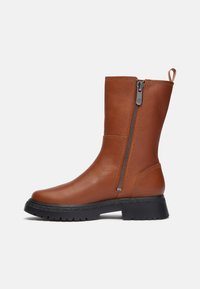 Stivale ankle in pelle marrone con zip laterale e superficie testurizzata. Presenta una suola nera spessa e un pull tab per una facile vestibilità. Finitura liscia.