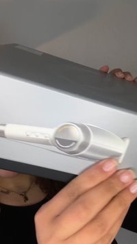 Hände halten eine schwarze Laptop-Box, die einen weißen Haartrockner mit einem kreisförmigen Steuerungswählrad in der Mitte zeigt.