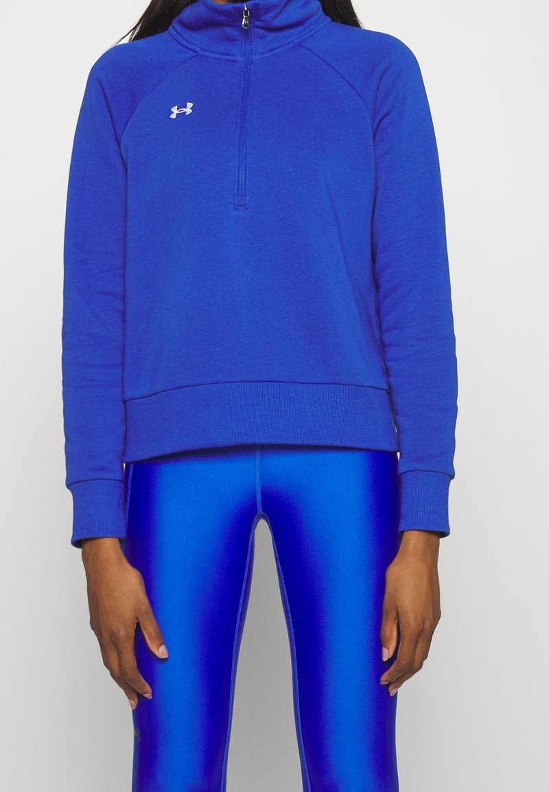 Sudadera de polar azul con cuello alto, cremallera de cuarto en la parte delantera y puños acanalados. Textura suave, combinada con leggings azules brillantes.