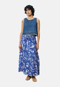 Denim crop top met uitgerafelde zoom, gecombineerd met een blauwe maxi rok met witte bloemmotieven. Model draagt beige instap schoenen.