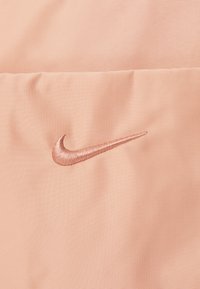 Nike sportkleding met een geweven, lichtroze stof en een geborduurd logo in een iets donkerdere roze tint. Gladde oppervlakte en zachte afwerking.